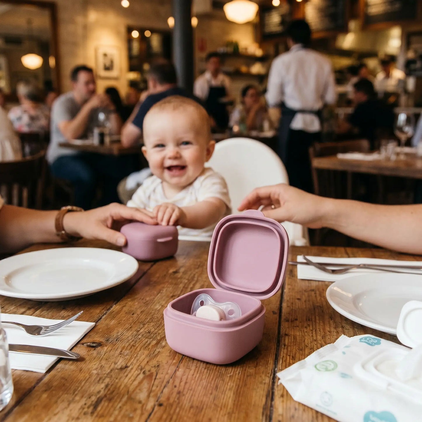 boite pour tetine posée sur la table du restaurant, bébé sourit