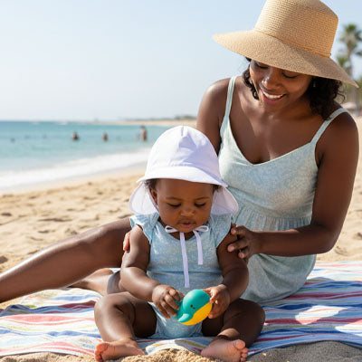 maman avec bébé à la plage bien protégé avec sa casquette pour bebe UV blanche