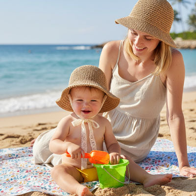 bébé qui porte son chapeau bebe à la plage avec maman