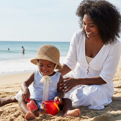 bébé qui porte son chapeau bebe à la plage avec maman