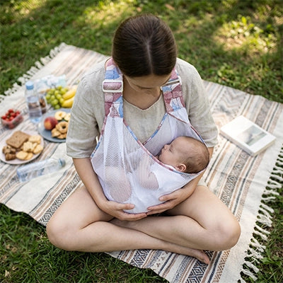 bébé dort dans son echarpe de portage physiologique dans les bras de maman au parc