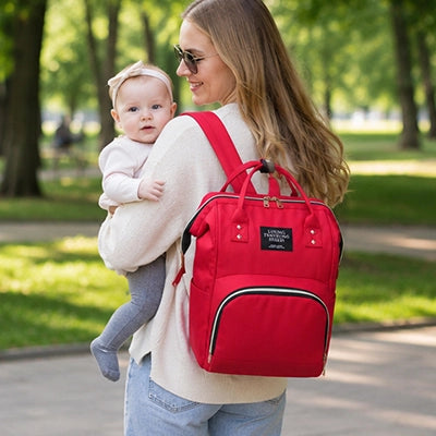 maman au parc avec bébé porte son sac a langer rouge