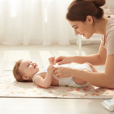 Maman change bébé sur son tapis à langer arc en ciel